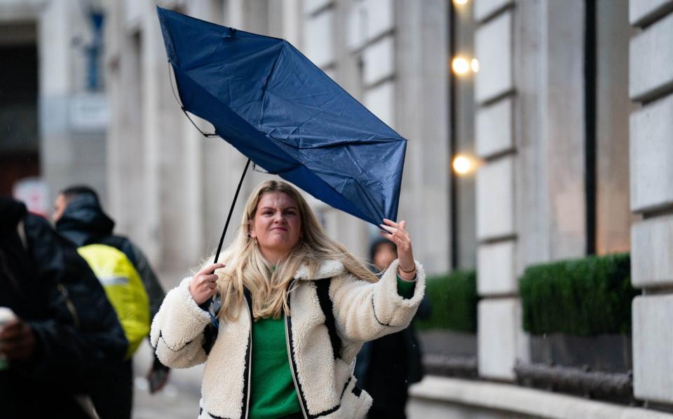 A young woman wrestles with her umbrella while walking in the rain near Aldwych, central London during Storm Jocelyn