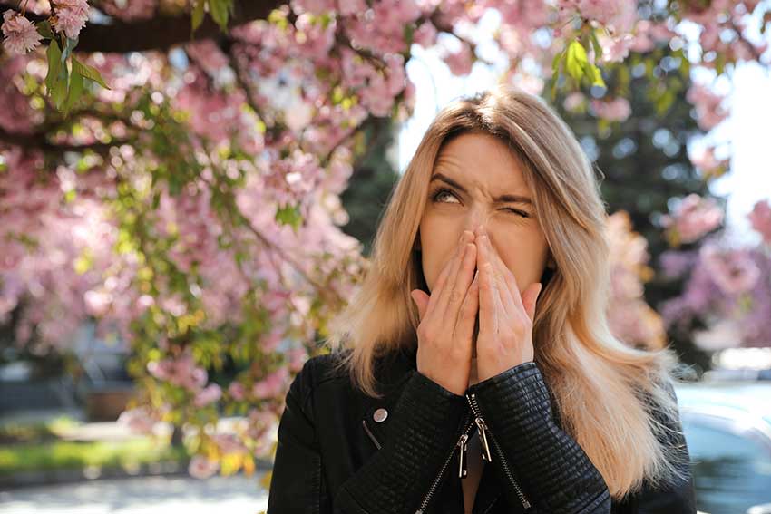 Mujer que sufre de alergia al polen estacional cerca de un árbol en flor al aire libre