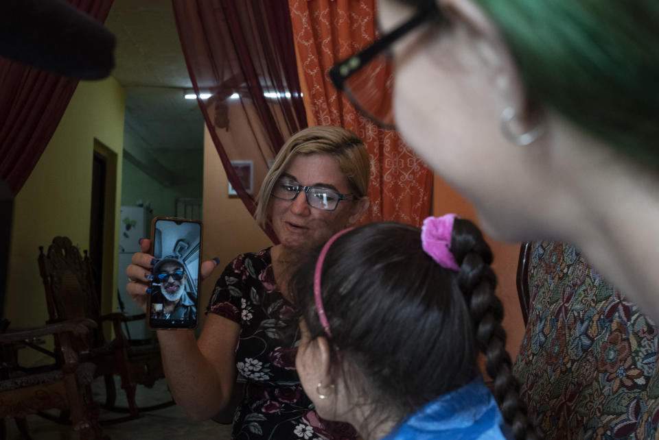 Danmara Triana holds her cell phone to show a live video image of her husband Roberto de la Iglesia, who has lived in the U.S. since 2015 with their son, during a video call with their daughters Alice and Claudia in Cienfuegos, Cuba, Thursday, May 19, 2022. Separated families see hope in the measures announced by the U.S. administration of President Joe Biden, but the long wait of years and a web of political interests also makes them skeptical. (AP Photo/Ramon Espinosa)