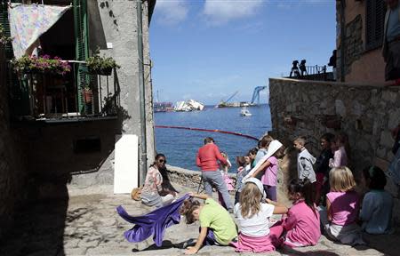 Children look on at the capsized Costa Concordia cruise liner (background) after the start of the "parbuckling" operation outside Giglio harbour September 16, 2013. REUTERS/Tony Gentile