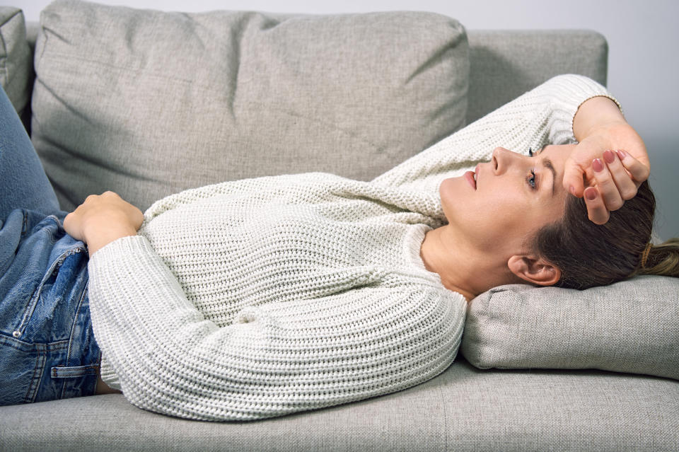 A woman lies on a sofa at home and hugs her stomach with her hands