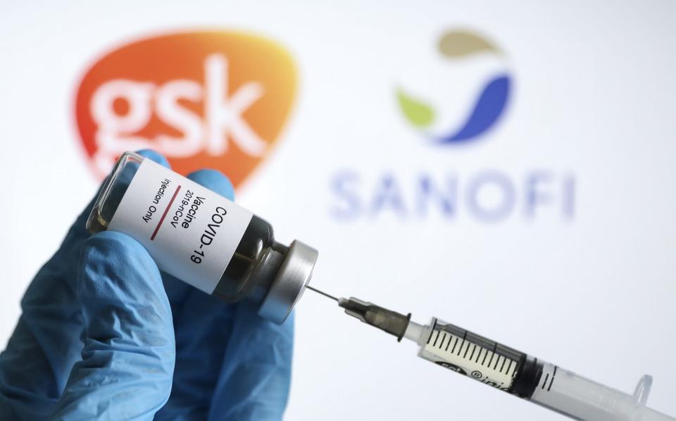 a vaccine syringe and a flacon are seen in front of a computer screen showing the GSK and Sanofi logos