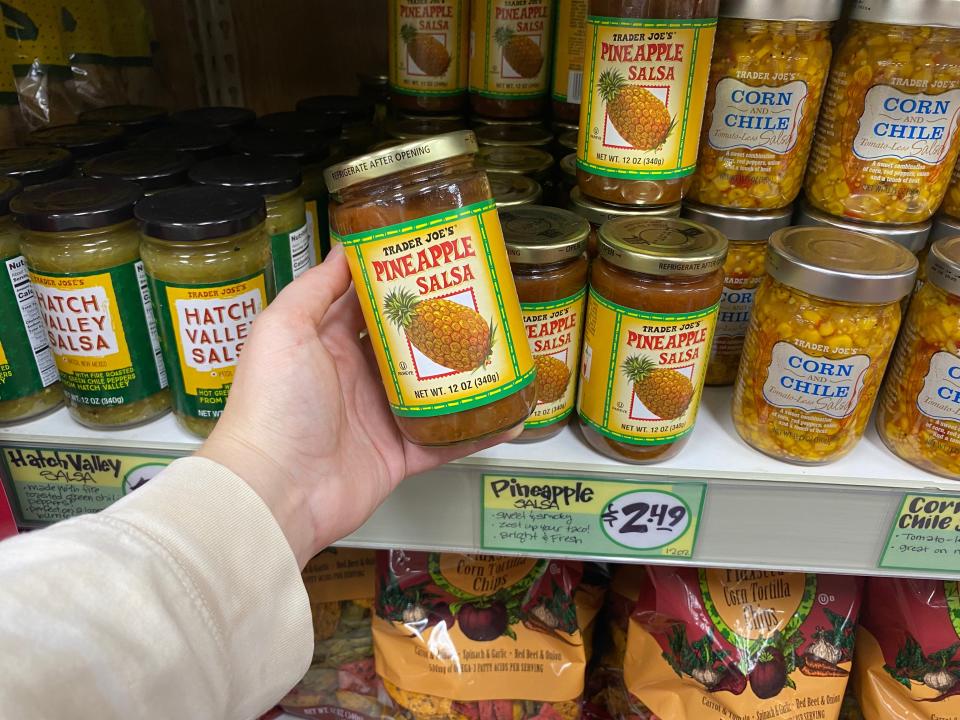 hand holding a jar of pineapple salsa in front of the salsa shelves at trader joes