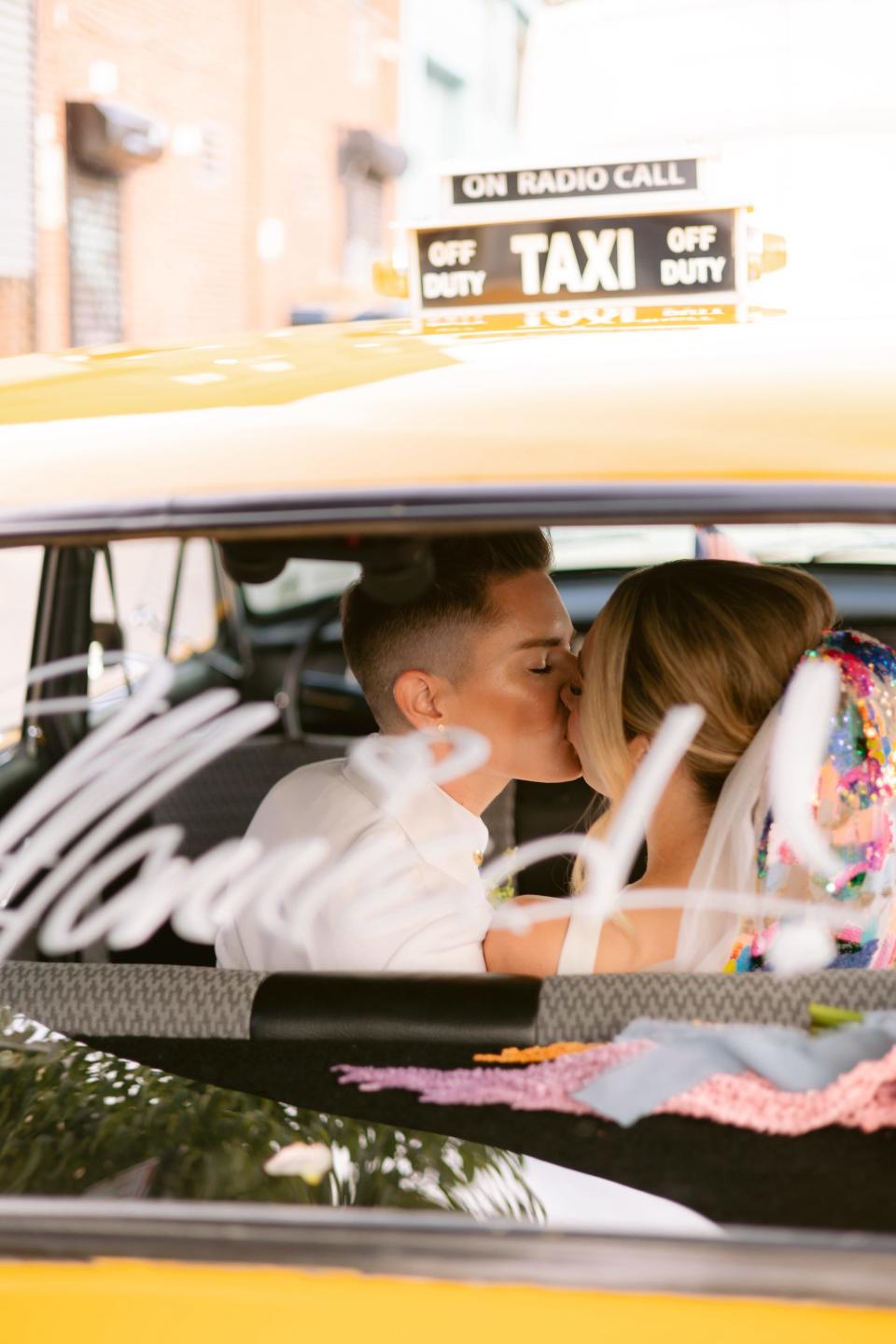 Two brides kiss in a taxi with 'just married!' written on the back window.