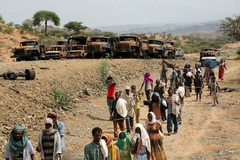 FILE PHOTO: Villagers return from a market to Yechila town in south central Tigray walking past scores of burned vehicles, in Tigray