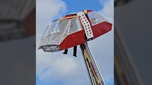 A ride operator dangles from a ride.