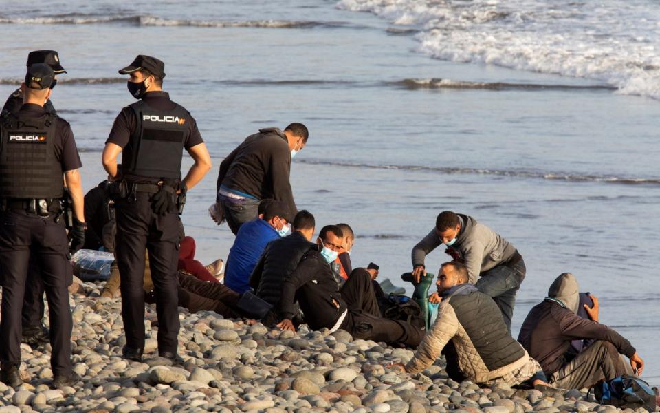 15 migrants wait on a shore as police officer approach to them in Gran Canaria   - Quique Curbelo/EPA-EFE/Shutterstock