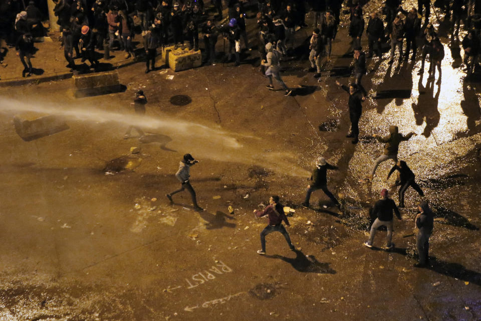 Anti-government protesters are sprayed by a water cannon as they throw stones at the riot police, during ongoing protests in front of the central government building in Beirut, Lebanon, Saturday, Jan. 25, 2020. Hundreds of Lebanese gathered outside the central government building to reject the newly formed Cabinet, while some protesters breached tight security erected around it, removing a metal gate and barbed wire prompting a stream of water cannons from security forces. (AP Photo/Bilal Hussein)