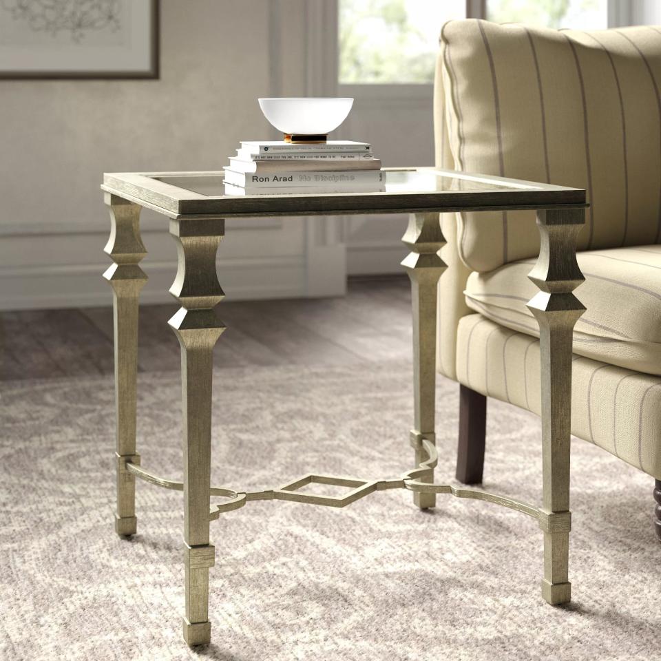 The square end table with a glass surface, silver frame and a cross design near the base in a living room