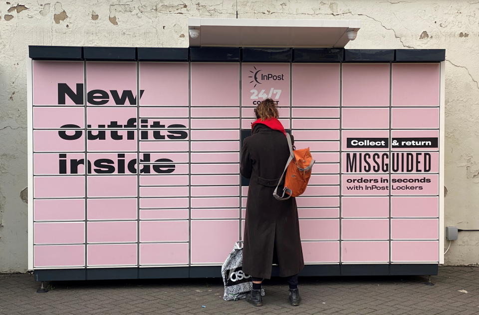 A woman stands at an InPost locker with an ASOS package at her feet in Hackney, London, Britain, January 26, 2021. REUTERS/Simon Newman