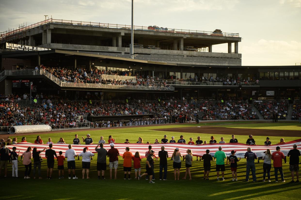 People carry out a large American flag onto the field during Fayetteville Woodpeckers' opening day at Segra Stadium on Thursday, April 18, 2019.