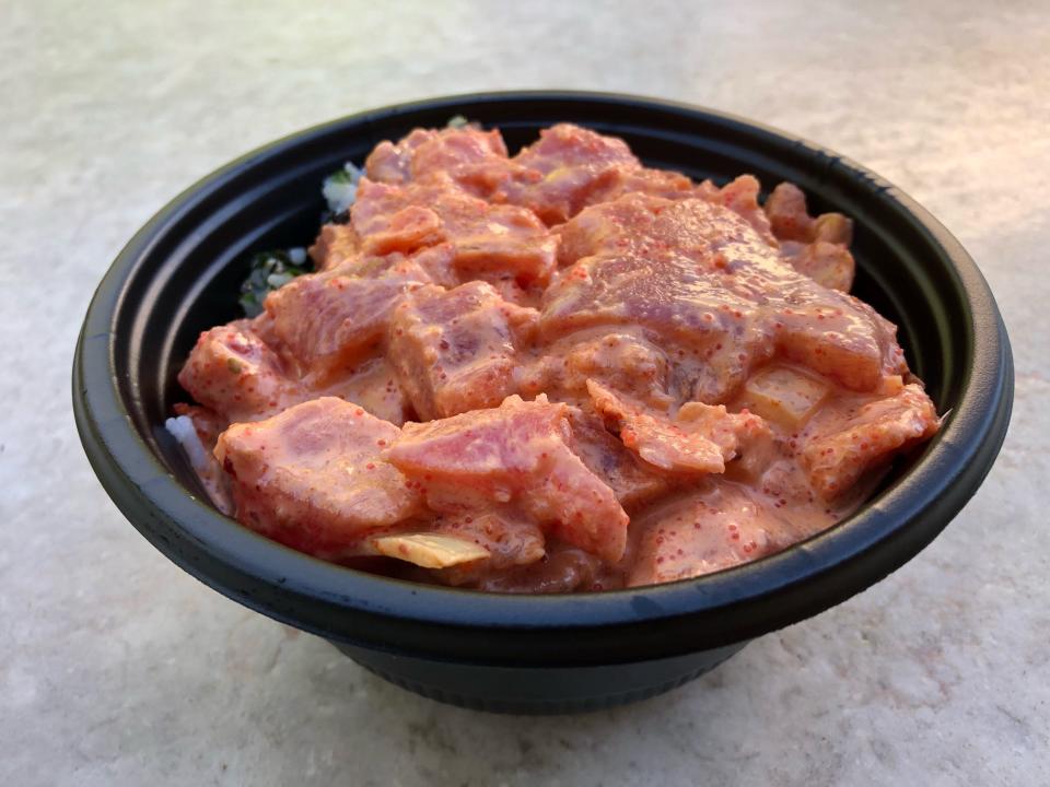 A spicy ahi poke bowl with the lid taken off, showing the raw, pink ahi in a mayo-based sauce