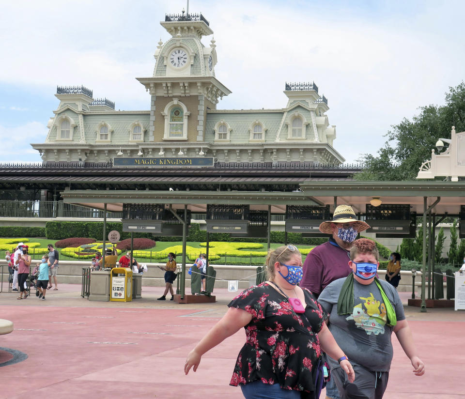 Guests wear masks as required to attend the official reopening day of the Magic Kingdom at Walt Disney World in Lake Buena Vista, Fla., Saturday, July 11, 2020. Disney reopened two Florida parks, the Magic Kingdom and Animal Kingdom, Saturday with limited capacity and safety protocols in place in response to the coronavirus pandemic. (Joe Burbank/Orlando Sentinel via AP)