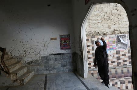 A policeman gestures beside a wall with shrapnel-scars, which witnesses said was damaged in a suicide blast on January 2015, in a Shi'ite mosque in Shikarpur, Pakistan March 19, 2017. Picture taken March 19, 2017. REUTERS/Akhtar Soomro