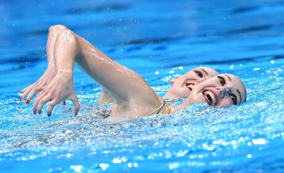 Two swimmers perfectly synchronized, with huge smiles on their faces and eyes wide open