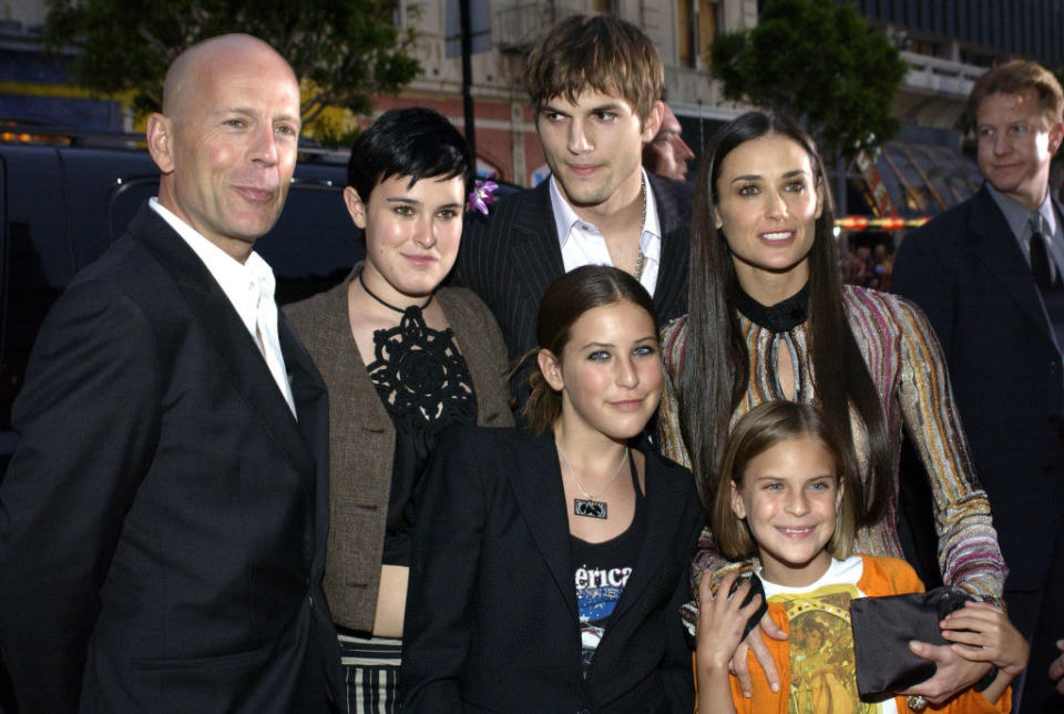 Ashton Kutcher while dating Demi Moore takes a picture with Demi's family and Bruce Willis, her ex; Ashton is staring at Bruce while everyone else smiles at the camera