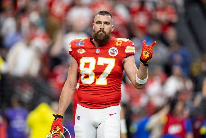 NFL player Travis Kelce in a red Kansas City Chiefs jersey with number 87, holding up two fingers on a stadium field during a game