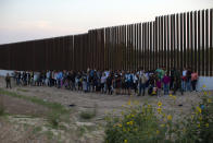 A group of migrants stand next to the border wall as they wait to get taken away by the Border Patrol in Eagle Pass, Texas, Saturday, May 21, 2022. The Eagle Pass area has become increasingly a popular crossing corridor for migrants, especially those from outside Mexico and Central America, under Title 42 authority, which expels migrants without a chance to seek asylum on grounds of preventing the spread of COVID-19. (AP Photo/Dario Lopez-Mills)