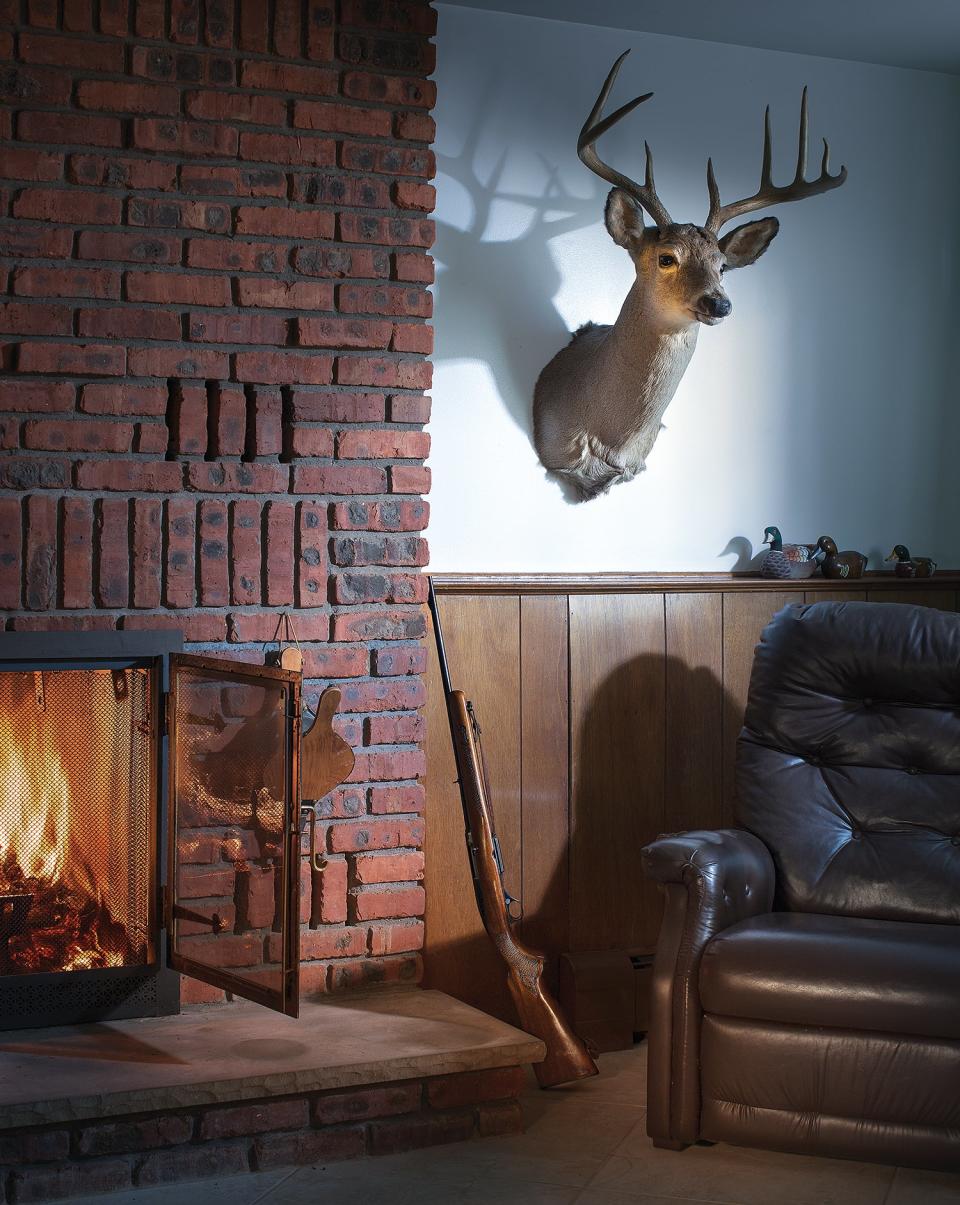 deer mount to the side of brick fireplace with roaring fire next to empty recliner