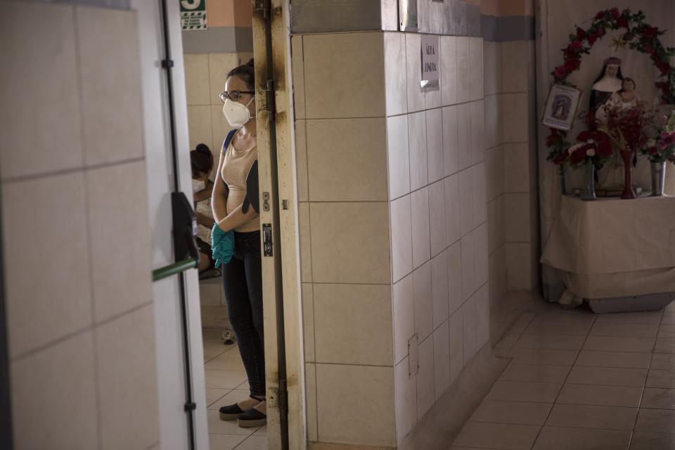 A relative, wearing a protective face mask and disposable gloves, waits for news on a family member outside an intensive care unit for people infected with the new coronavirus, at the 2 de Mayo Hospital, in Lima, Peru, Friday, April 17, 2020. (AP Photo/Rodrigo Abd)