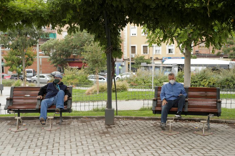 People wearing protective face masks sit at benches at Carabanchel neighbourhood in Madrid