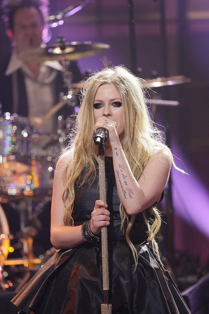 Singer Avril Lavigne with microphone performing on stage, drummer in background