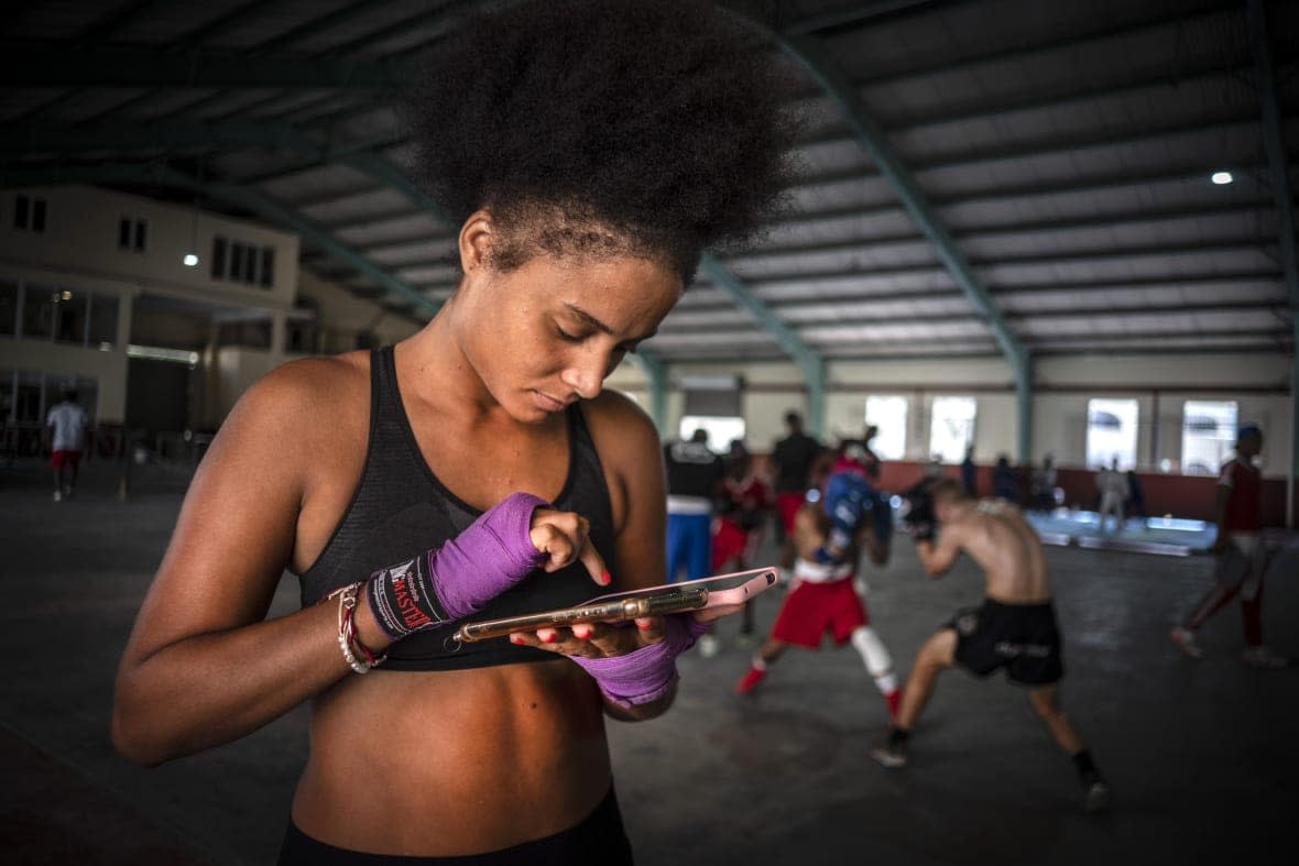 Boxer Giselle Bello Garcia texts on a mobile phone while other athletes train at a boxing gym in Havana, Cuba, Monday, Dec. 5, 2022. Cuban officials announced on Monday that women boxers would be able to compete for the first time ever. (AP Photo/Ramon Espinosa)