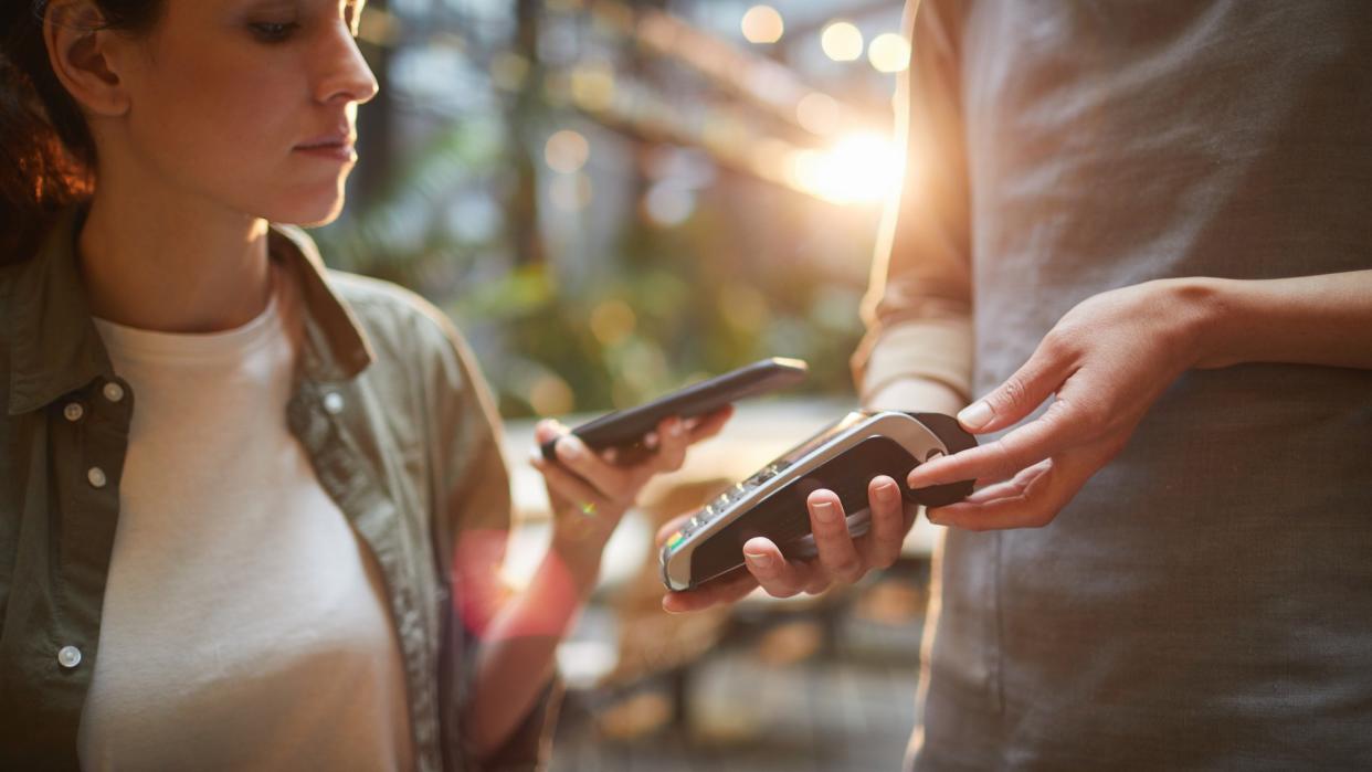 Cropped portrait of young woman paying via NFC in cafe, focus on female hands holding banking terminal, copy space.