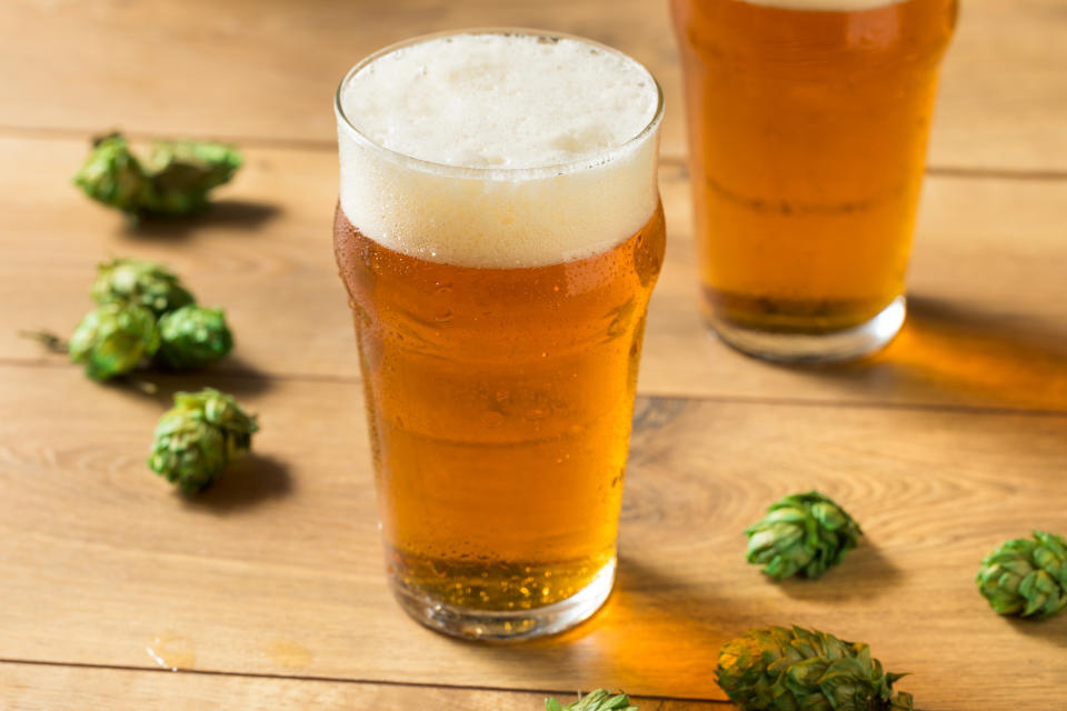 Two glasses of beer on a wooden table, surrounded by scattered hops