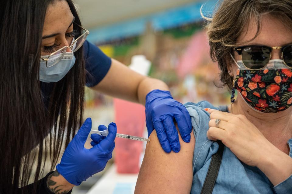 Women with mask and glasses administers COVID-19 vaccine to middle-aged women with sunglasses and patterned mask