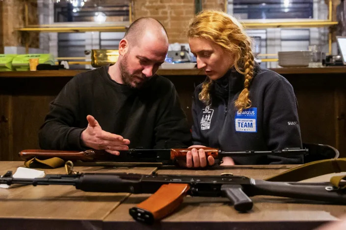 A member of Ukraine’s Territorial Defense Forces holds a Kalashnikov rifle as a volunteer looks on.