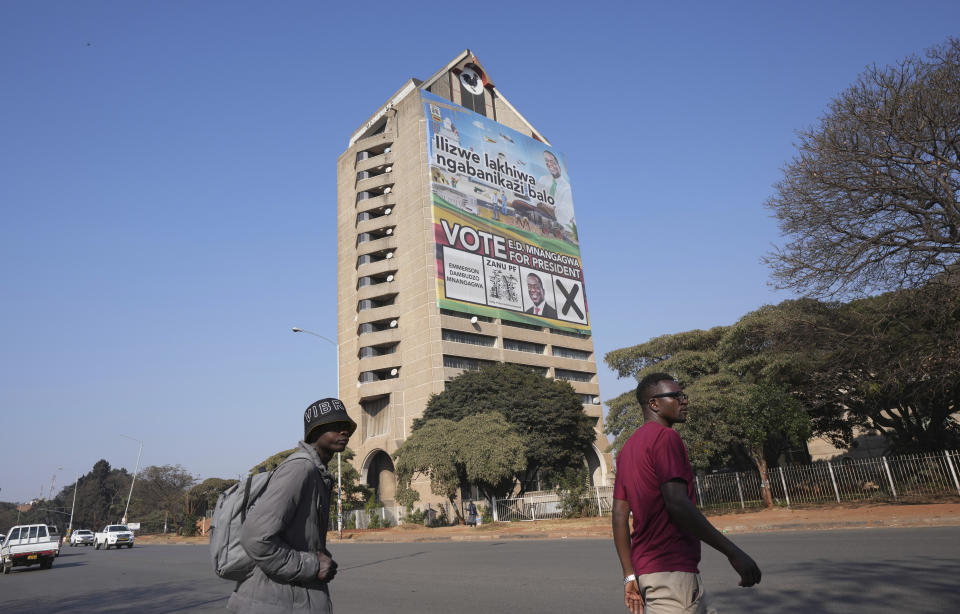 Pedestrians cross a road passing the ruling ZANU PF headquarters displaying a portrait of Zimbabwe's President Emmerson Mnangagwa, in Harare, Sunday Aug. 20, 2023. 80-year-old Mnangagwa is now seeking re-election for a second term as president in a vote this week that could see the ruling ZANU-PF party extend a 43-year hold on power. (AP Photo/Tsvangirayi Mukwazhi)