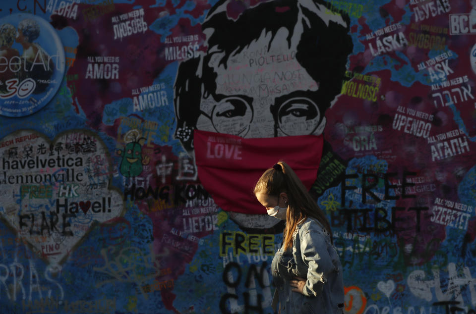 A woman passes by the "Lennon Wall" with a face mask attached to the image of John Lennon, in Prague, Czech Republic, Monday, April 6, 2020. The Czech Republic's government has incorporated dramatic restrictive measures to try and stem the spread of the new coronavirus. (AP Photo/Petr David Josek)