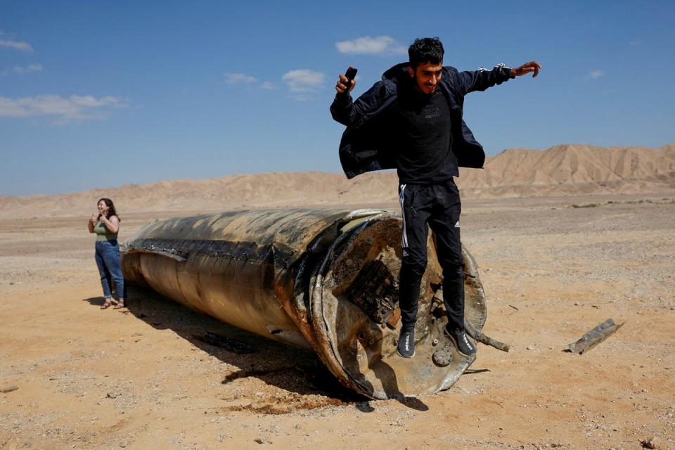 A man jumps off apparent remains of a ballistic missile lying in the desert, following an attack by Iran on Israel (Reuters)