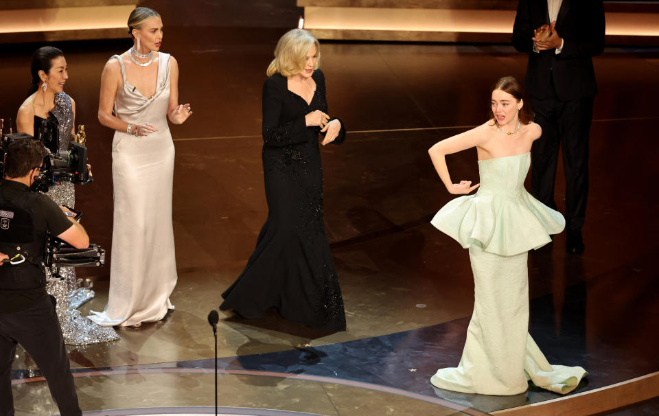 Emma Stone gestures toward her dress as she wins the Oscar for Best Actress for 