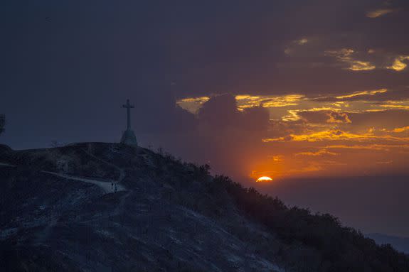 A couple survey the damage as they walk near a cross that remains standing amid the scorched hillside that destroyed three buildings on September 3, 2017.