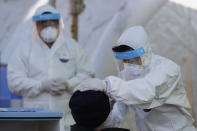 A medical worker wearing protective gear takes a sample from a man at a coronavirus/COVID-19 testing site in Seoul, South Korea, Sunday, Dec. 20, 2020. (AP Photo/Lee Jin-man)