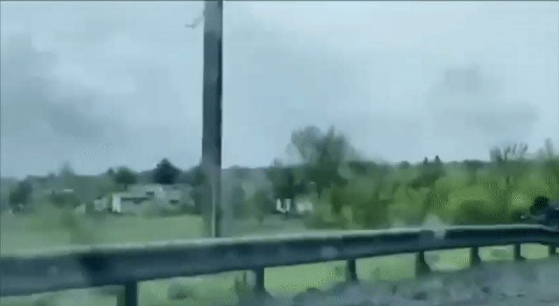 Video from inside a car showing destruction along a muddy road in the rain.