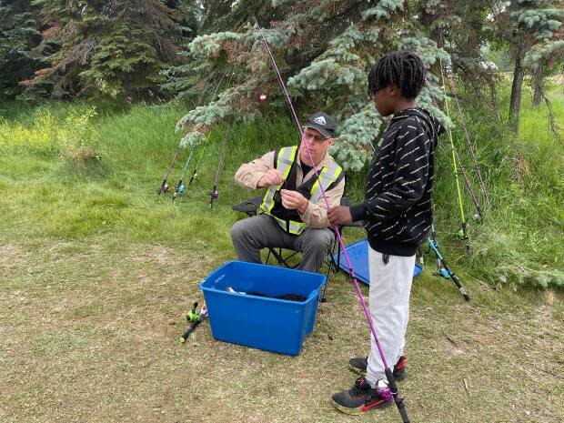 A supervisor gets bait on a line for a child learning to fish for the first time in Edmonton on Saturday. (Emily Fitzpatrick/CBC - image credit)