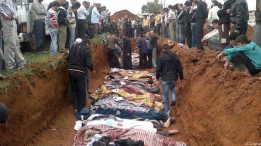 A picture released by the Local Coordination Committees in Syria (LCC) purportedly shows people standing around a mass grave in the town of Taftnaz on April 5, as bodies are laid out for burial in Idlib province. AFP cannot independently verify this image. Syria says it will not withdraw from protest hubs without written guarantees from the opposition groups