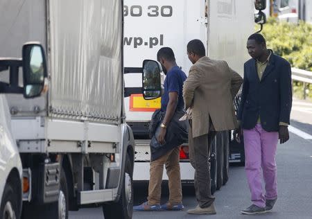 Migrants check the trailer of a truck during an attempt to make a clandestine crossing to England through the Channel tunnel as lorries wait on a road which leads to the Channel Tunnel terminal in Coquelles near Calais, northern France, July 1, 2015. REUTERS/Vincent Kessler