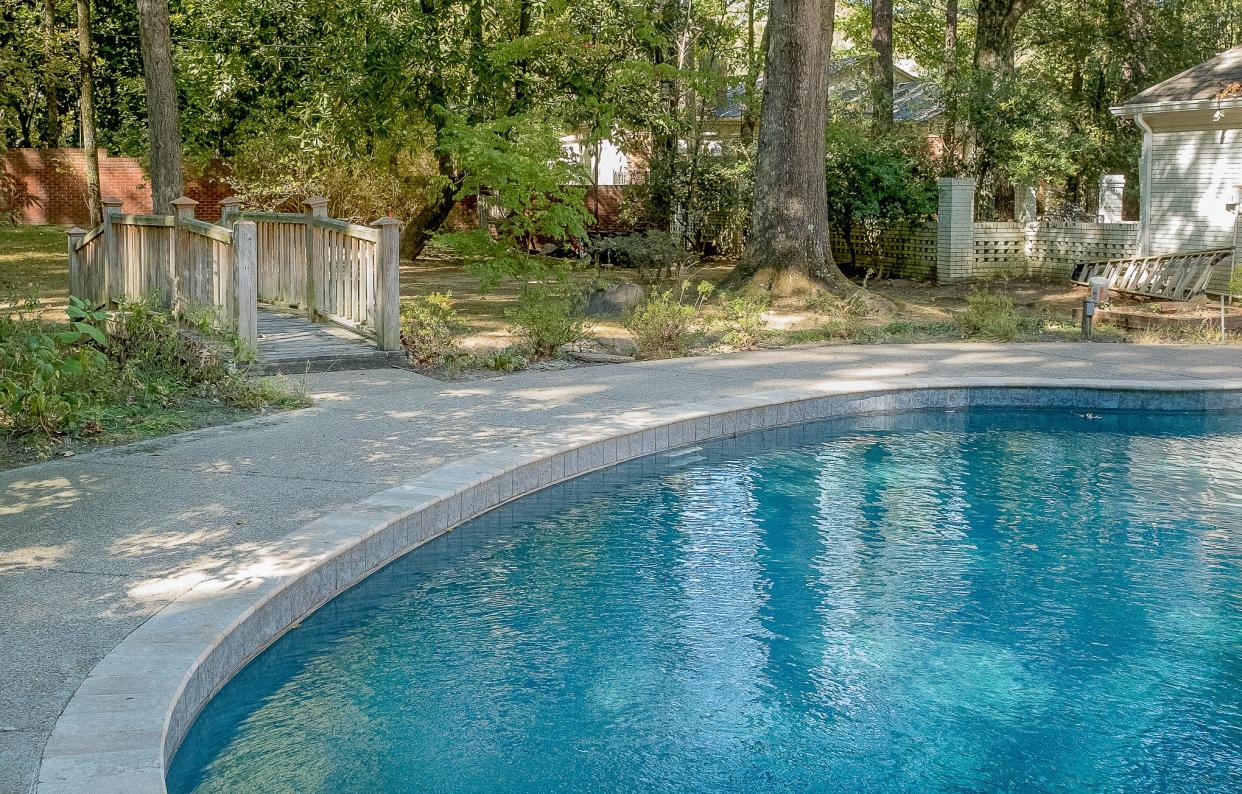 The backyard features a pool surrounded by lush, wooded landscaping and a footbridge that allows an easy transition from one area of the yard to another.