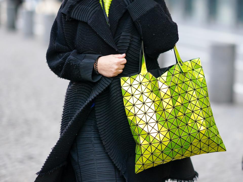 A guest wears a neon yellow pullover, a long oversized black striped rib jacket, a black set stripped pants, a yellow neon Bao Boa Issey Miyake handbag, outside Berluti, during Paris Fashion Week - Menswear F/W 2020-2021 on January 17, 2020 in Paris, France.