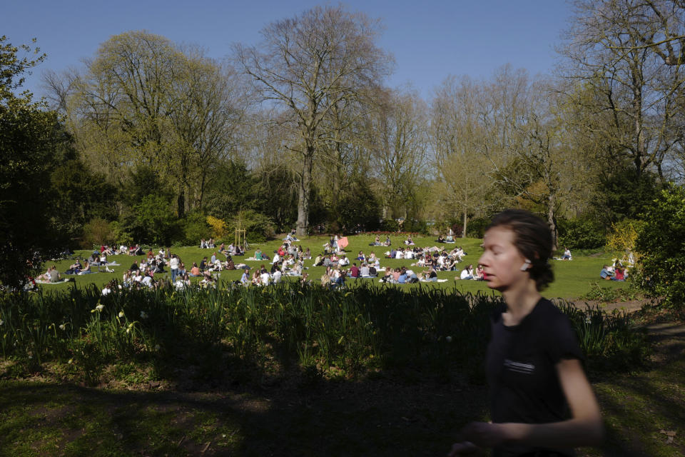 A woman jogs as people sit in the Vauban park in Lille, northern France, Tuesday, March 30, 2021. The number of patients in intensive care in France on Monday surpassed the worst point of the country's last coronavirus surge in the autumn of 2020, another indicator of how a renewed crush of infections is bearing down on French hospitals. (AP Photo/Michel Spingler)