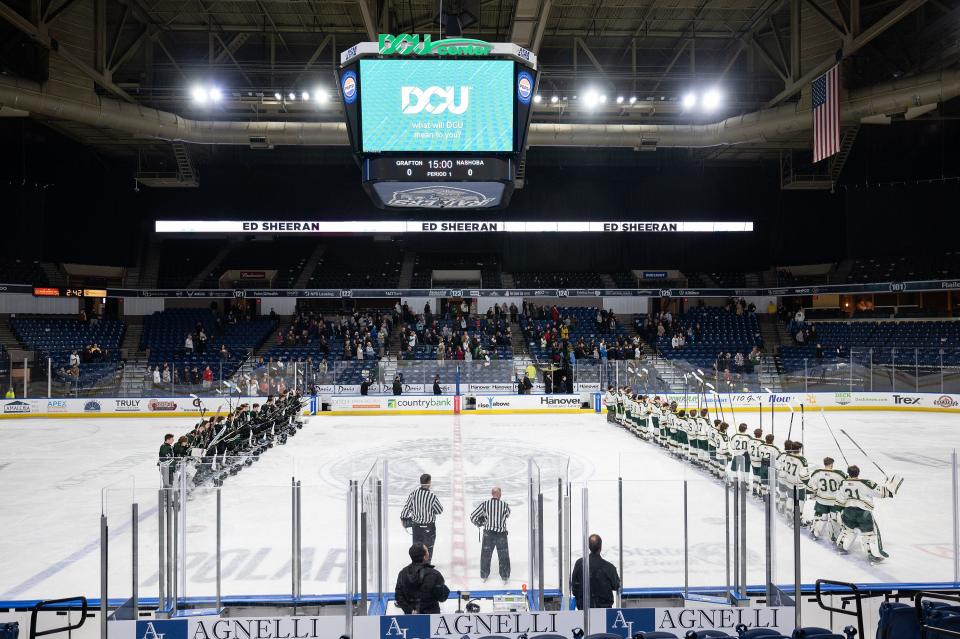 Grafton and Nashoba players raise their sticks at the end of the national anthem Saturday at the DCU Center.