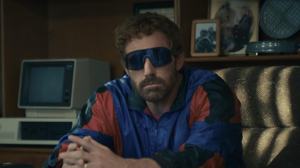 Ben Affleck sits at a desk, wearing shades and a track suit, in Air.