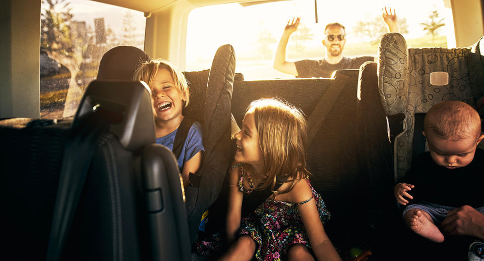 Shot of adorable little children sitting in a car and a dad closing the boot.