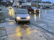 A car collided with a pole near downtown Bismarck, N.D., on Tuesday morning, Dec. 26, 2023, as ice covered streets and sidewalks made walking and driving difficult. (Tom Stromme/The Bismarck Tribune via AP)