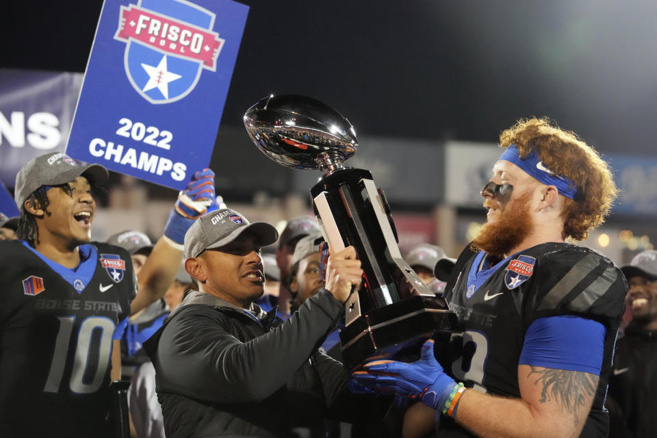 Boise State head coach Andy Avalos, center, hands the trophy to defensive tackle Scott Matlock (99) as quarterback Taylen Green (10) looks on after they beat North Texas and winning the Frisco Bowl NCAA college football game Saturday, Dec. 17, 2022, in Frisco, Texas. (AP Photo/LM Otero)