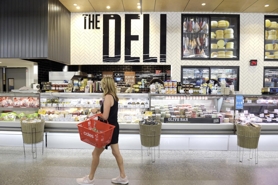 Una donna cammina vicino a un negozio di gastronomia Coles portando un cestino rosso in braccio.  Fonte: Getty